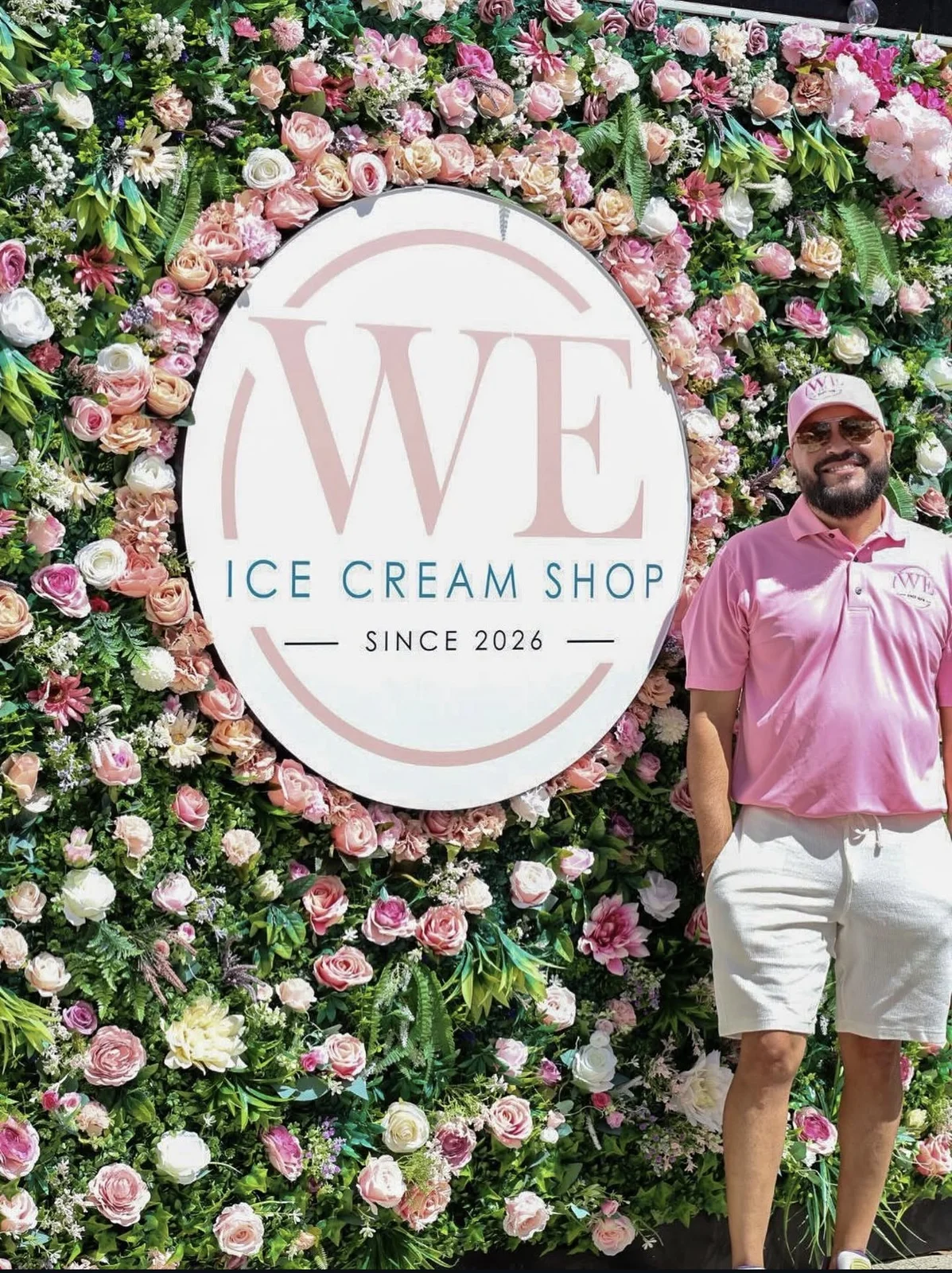 El dueño de WE Ice Cream Shop junto al logo en el mural de flores